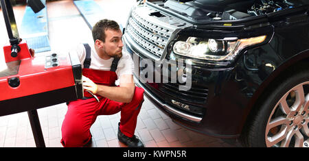 Riparazione auto shop - lavoratore controlla e regola i fari di un'auto del sistema di illuminazione Foto Stock