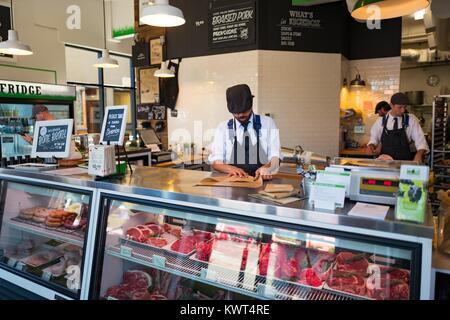 Un uomo che indossa un grembiule a strisce e hat esegue il wrapping di un pezzo di carne, con molti tagli di carne rossa visibile in una vetrina a livello locale macelleria, un artigiano macelleria nel Ghetto Gourmet (Nord Shattuck) quartiere di Berkeley, California, 27 settembre 2017. () Foto Stock