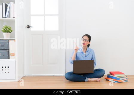 Attraente donna seduta sul pavimento di legno di casa utilizzando computer facendo studiare i compiti aventi una buona idea con sfondo bianco. Foto Stock