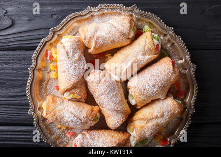 Cannoli dolce farcito con crema di formaggio e frutta candita close-up su una piastra su un tavolo. parte superiore orizzontale vista da sopra Foto Stock