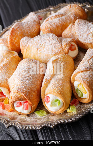 Dolce siciliano di rotoli di cannoli con crema di formaggio e frutta candita close-up su una piastra verticale. Foto Stock