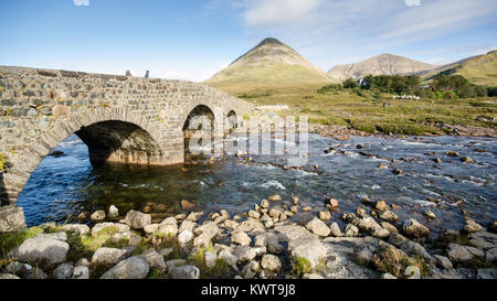 Antico arco in pietra ponte su un fiume di montagna a Sligachan sull'Isola di Skye nelle Highlands della Scozia, con le montagne del Cuillin rising essere Foto Stock