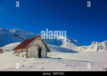 Paesaggio invernale con legno toolshed e Monti Fagaras ricoperto di uno strato spesso di neve al lago Balea, contea di Sibiu, Romania Foto Stock