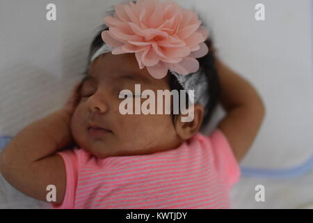 Neonato ragazza in rosa dorme tranquillamente sulla sua schiena con le braccia attorno alla sua testa Foto Stock