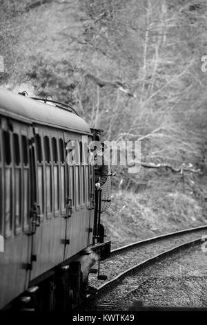 In bianco e nero ritratto di muoversi UK treno a vapore sulla via della ferrovia del patrimonio. Driver del treno si affaccia di locomotiva, quasi nascosto dietro il carrello. Foto Stock