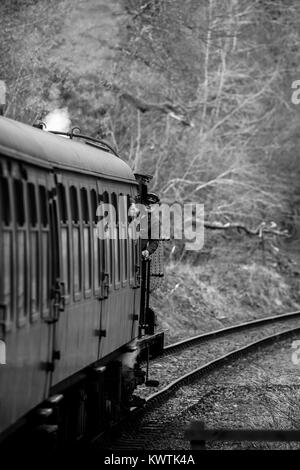 In bianco e nero ritratto di muoversi UK treno a vapore sulla via della ferrovia del patrimonio. Driver del treno si affaccia di locomotiva, quasi nascosto dietro il carrello Foto Stock