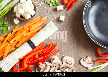 Vegetariano vegano cibo asiatico ingredienti per friggere con tofu, tagliatelle, funghi e verdure sopra lo sfondo di legno con copia spazio.