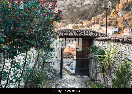 Berat, città storica nel sud dell'Albania, in vista della città attraverso un aperto vecchia porta di legno. Giardino privato, cancelli, muri in pietra e una vista per fam Foto Stock