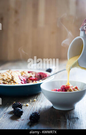 Crema pasticcera calda che viene versato nel corso della cottura a vapore la frutta crumble Foto Stock