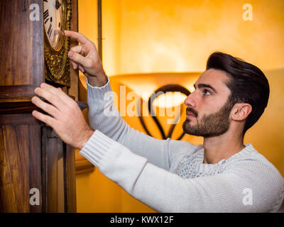Vista laterale del giovane uomo bello permanente e la impostazione vintage orologio a pendolo. Foto Stock