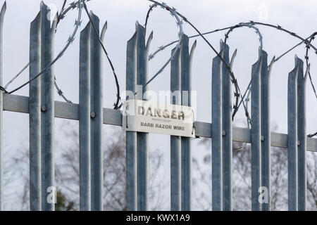 Picchi in acciaio galvanizzato sulla parte superiore di un cancello di sicurezza o recinto e rabboccato con filo spinato filo di rasoio con un avviso di pericolo Foto Stock