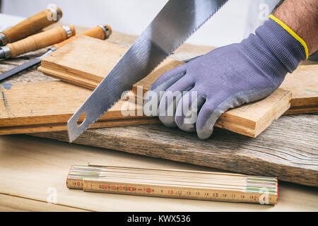 L'uomo con i guanti lavora con una sega a mano Foto Stock