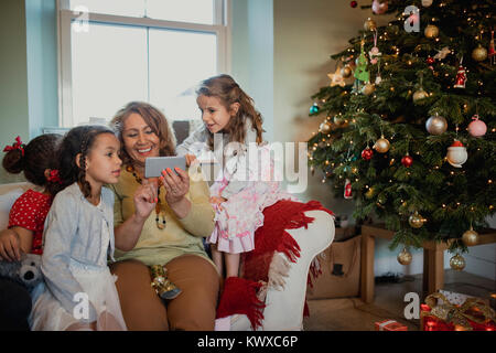 Una nonna si divertono su uno smart phone con il suo granddughters al tempo di Natale. Foto Stock