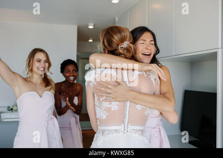 Felice bridesmaids congratularmi con sposa in abito da sposa in camera d'albergo. Bridesmaids abbracciando la sposa e sorridente. Foto Stock