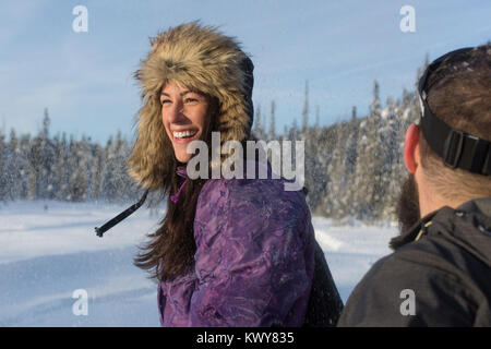 Donna sorridente con cappello di pelliccia attiva all'aperto in inverno con alberi ricoperti di neve Foto Stock
