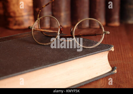 Primo piano di molto vecchi occhiali giacente sul libro sullo sfondo con scaffale Foto Stock