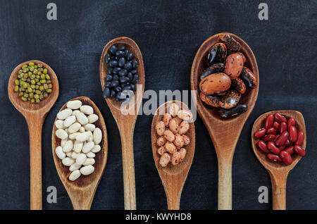 Vari i fagioli in cucchiai di legno su sfondo nero Foto Stock