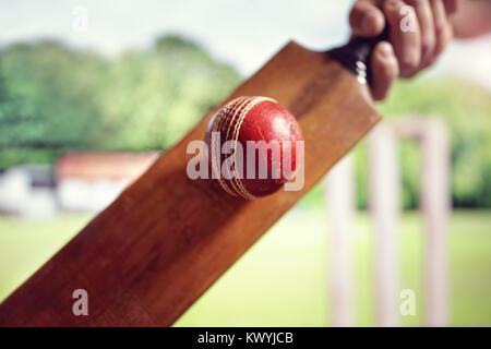 Cricket battitore di colpire una pallina colpo da sotto con monconi sul campo da cricket Foto Stock