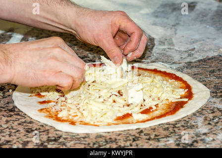 Freschi e originali Italian pizza cruda, pasta di preparazione in tradizionale stile: lo chef distribuisce il formaggio. Il cibo e la cucina italiana e il concetto di cucina a vista. Foto Stock