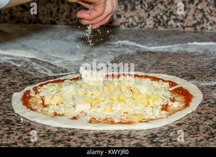 Freschi e originali Italian pizza cruda, pasta di preparazione in tradizionale stile: lo chef distribuisce il formaggio. Il cibo e la cucina italiana e il concetto di cucina a vista. Foto Stock