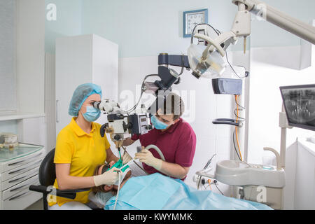 Professional dentista esame paziente con microscopio presso l'ufficio. Il dentista e l'assistente sono il trattamento di denti per il paziente Foto Stock