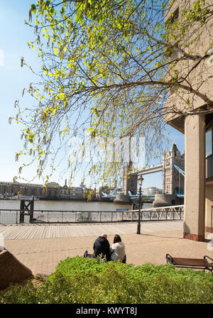 LONDON, Regno Unito - 16 Aprile 2014: giovane seduto sul banco sul lungofiume da Tower Bridge, godendo il sole caldo nel mese di aprile Foto Stock