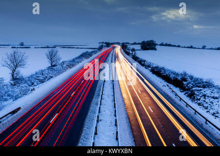 Sentieri di luce delle vetture in movimento sulla autostrada rurale nella neve in inverno. Foto Stock