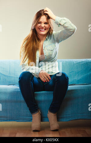 Giovani concetto - funny capelli lunghi rendendo ragazza sciocca faccia seduti sul divano giovane donna di graffiare la testa, pensando fantasticando su qualcosa di Foto Stock