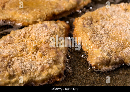 La frittura Wiener Schnitzel in una padella calda con olio di cottura Foto Stock