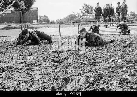 Esercito britannico squaddies sottoposti a formazione di base strisciare attraverso il fango sotto il filo spinato come parte di un percorso ad ostacoli. In Inghilterra. 15 Giugno 1993 Foto Stock