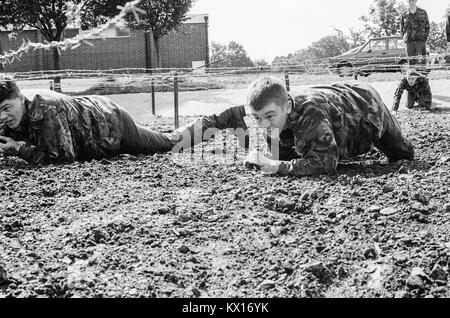 Esercito britannico squaddies sottoposti a formazione di base strisciare attraverso il fango sotto il filo spinato come parte di un percorso ad ostacoli. In Inghilterra. 15 Giugno 1993 Foto Stock