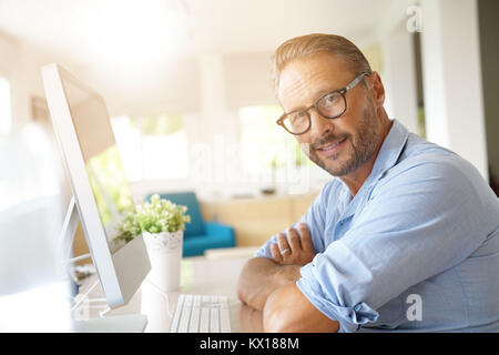 Uomo maturo che lavorano da casa su computer desktop Foto Stock