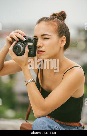 Eurasian (metà europeo, metà asiatica) ragazza si inginocchia per scattare una fotografia con la sua fotocamera polaroid in Bangkok, Tailandia Foto Stock