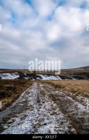 Lammermuir Hills, East Lothian, Scozia, Regno Unito. Un uomo con uno zaino cammina lungo una pista umida della brughiera. La neve si trova sulla brughiera in una fredda giornata invernale Foto Stock