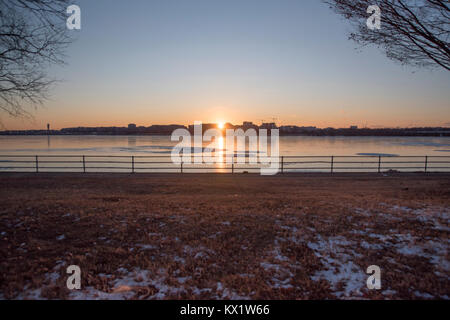 Washington DC, Stati Uniti d'America . 06 gen 2018. Il fiume Potomac al punto Hains nell est del Potomac Park, Washington DC riflette il sole al tramonto sul suo parzialmente congelati superficie. La città di cristallo può essere visto di profilo attraverso l'acqua. Credito: Angela Drake/Alamy Live News Foto Stock