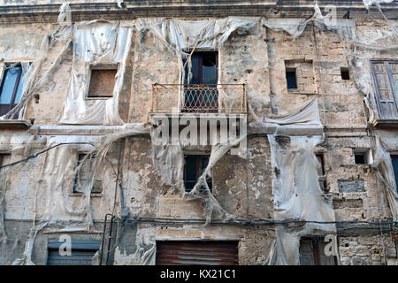 Particolare della facciata di un vecchio e un edificio abbandonato di Trapani, in Sicilia (Italia) con filamenti di teloni di plastica sopra le finestre. Foto Stock