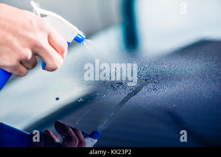 Spruzzatura manuale sostanza detergente sulla superficie di un auto blu Foto Stock