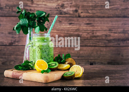 Delizioso Frullato di kiwi con la menta in mason jar sul tavolo contro il legno scuro dello sfondo. Uno stile di vita sano concetto Foto Stock