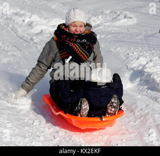 Un sorridente giovane madre lo slittino con il suo bambino (1 yr old) figlia Foto Stock