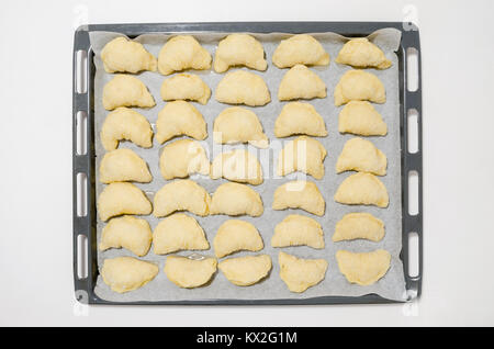 Vista superiore piana dei laici insieme di dolci fatti in casa il lievito croissant durante la preparazione- posa sulla carta da forno su metallo forno- pronti per la cottura. Foto Stock