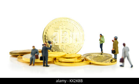 Primo piano della golden bitcoin moneta su sfondo bianco con molte monete d oro a fondo e statuine in miniatura in piedi intorno Foto Stock