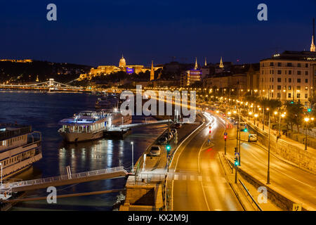 La città di Budapest di notte in Ungheria, street e navi da crociera sul fiume Danubio sul lato di Buda, vista verso il castello. Foto Stock