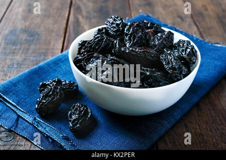 Le prugne secche in una ciotola di ceramica su legno scuro dello sfondo. Frutta secca. Foto Stock