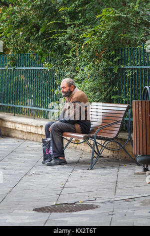 Tipico giù e fuori povero vecchio uomo seduto su una panchina a bordo strada mendicando da passanti a Bucarest, la capitale della Romania, Europa centrale Foto Stock