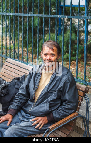 Tipico giù e fuori povero vecchio uomo seduto su una panchina a bordo strada mendicando da passanti a Bucarest, la capitale della Romania, Europa centrale Foto Stock