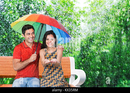 2 giovane sotto ombrellone seduta panchina nel parco di estate Fun-Enjoy pioggia Foto Stock