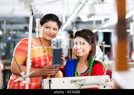 2 Donne Lavoratori collega sarto s lettura del testo- Messaggio SMS cucitura telefono -Factory Foto Stock