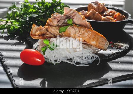 Il cellophane con un pezzo di salmone arrosto con i pomodori, la cipolla e il prezzemolo nel Consiglio di Amministrazione di nero ardesia. Close-up. Foto Stock