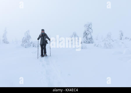 Un caldo vestito donna escursionismo attraverso la fresca artico bianco neve con le racchette da neve in una fredda giornata invernale. Riisitunturi, Ruka, Finlandia. Foto Stock