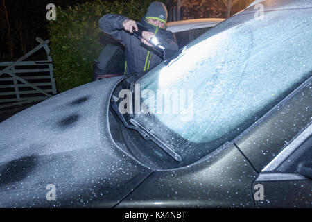 Lixwm, Flintshire, Galles . Regno Unito Meteo. Anrapid dignitoso a temperatura ha lasciato un grave gelo per tutta la notte in molte parti del Regno Unito tra cui il villaggio di Lixwm in Flintshire come un " commuter " mattina inizia a raschiare il ghiaccio di un parabrezza di automobile vestito per il freddo Foto Stock